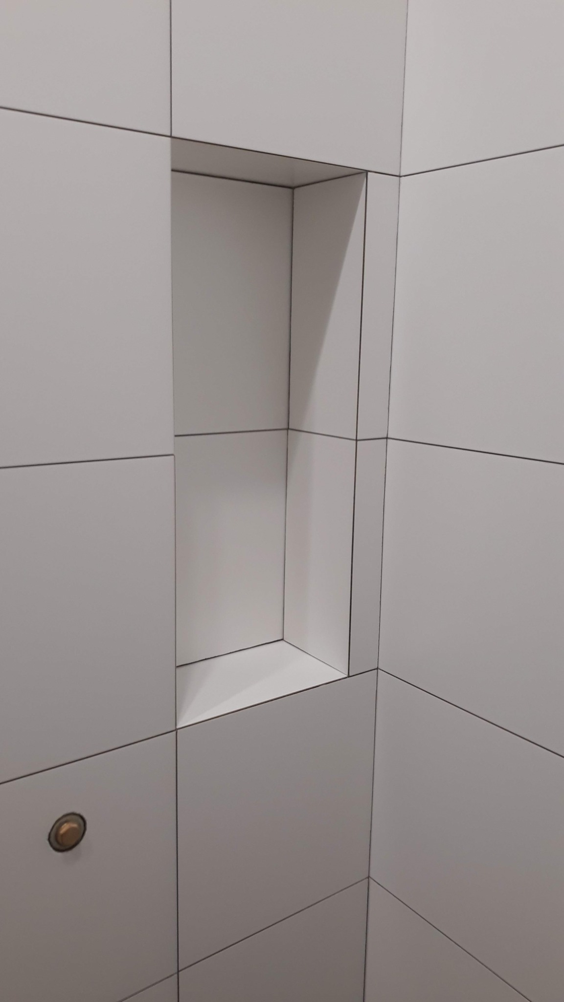 Białe płytki w łazience z wnęką w ścianie, oświetlenie punktowe w jednej z płytek.