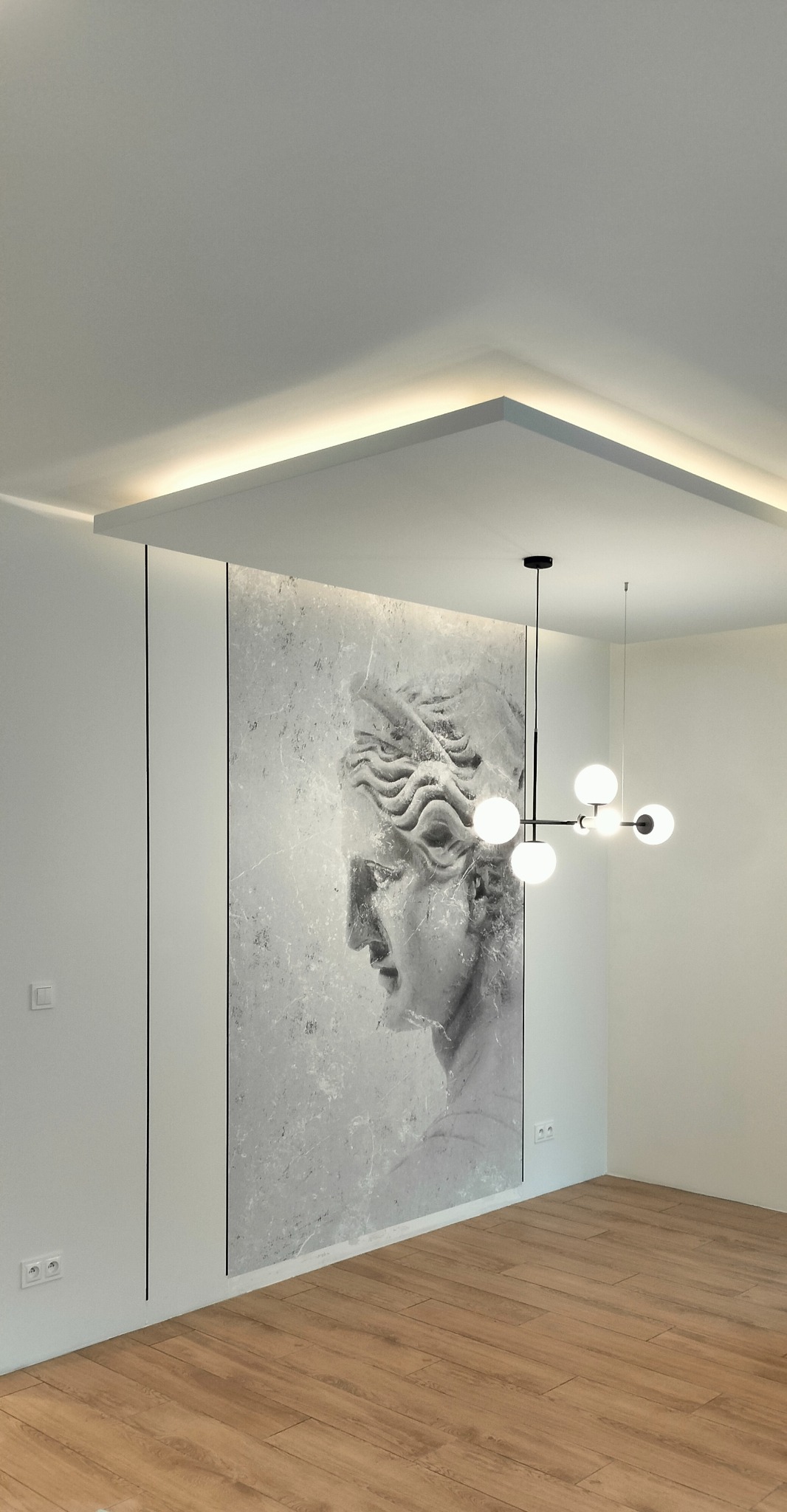 Nowoczesne wnętrze z drewnianą podłogą, minimalistycznym oświetleniem sufitowym i dekoracyjnym panelem ściennym z wizerunkiem antycznej rzeźby.