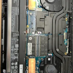 Wnętrze laptopa HP Victus z widoczną baterią, dwoma wentylatorami chłodzącymi, modułami RAM Goodram, płytą główną oraz układem chłodzenia z rurkami cieplnymi.