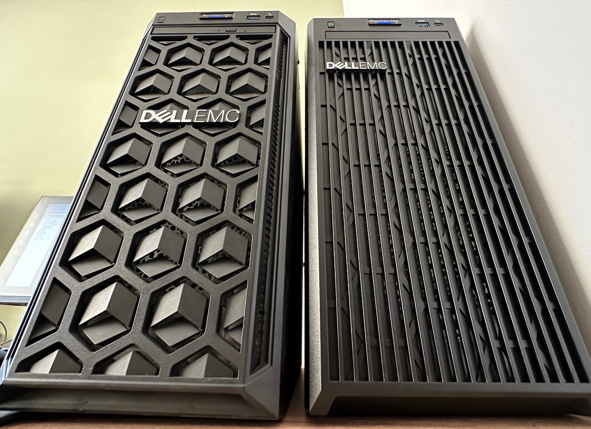 Dwa serwery Dell EMC PowerEdge T140 i T150 stojące obok siebie, z różnymi wzorami perforacji na przednich panelach: jeden z geometrycznym wzorem plastra miodu, drugi z pionowymi żebrami.