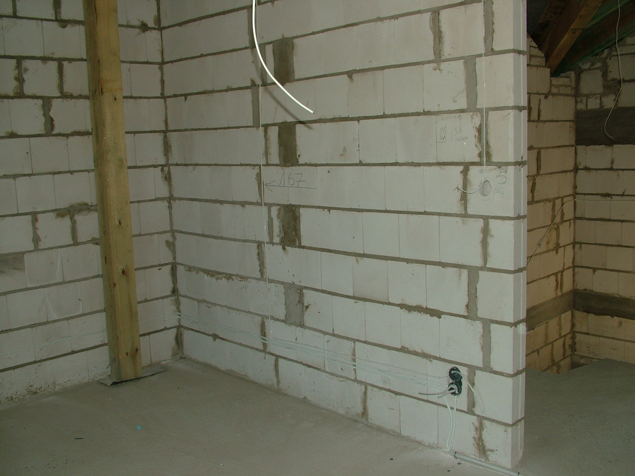 Wnętrze w trakcie budowy: ściany z betonu komórkowego z widocznymi przewodami elektrycznymi i puszkami instalacyjnymi pod gniazdka. Surowy stan, brak wykończenia.