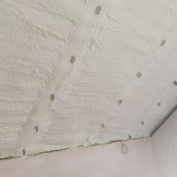 KONS-MET Łukasz Grejber - Poddasze po natrysku pianki izolacyjnej, widoczne otwory po kołkach montażowych, w rogu pomieszczenia logo firmy X-TERM.