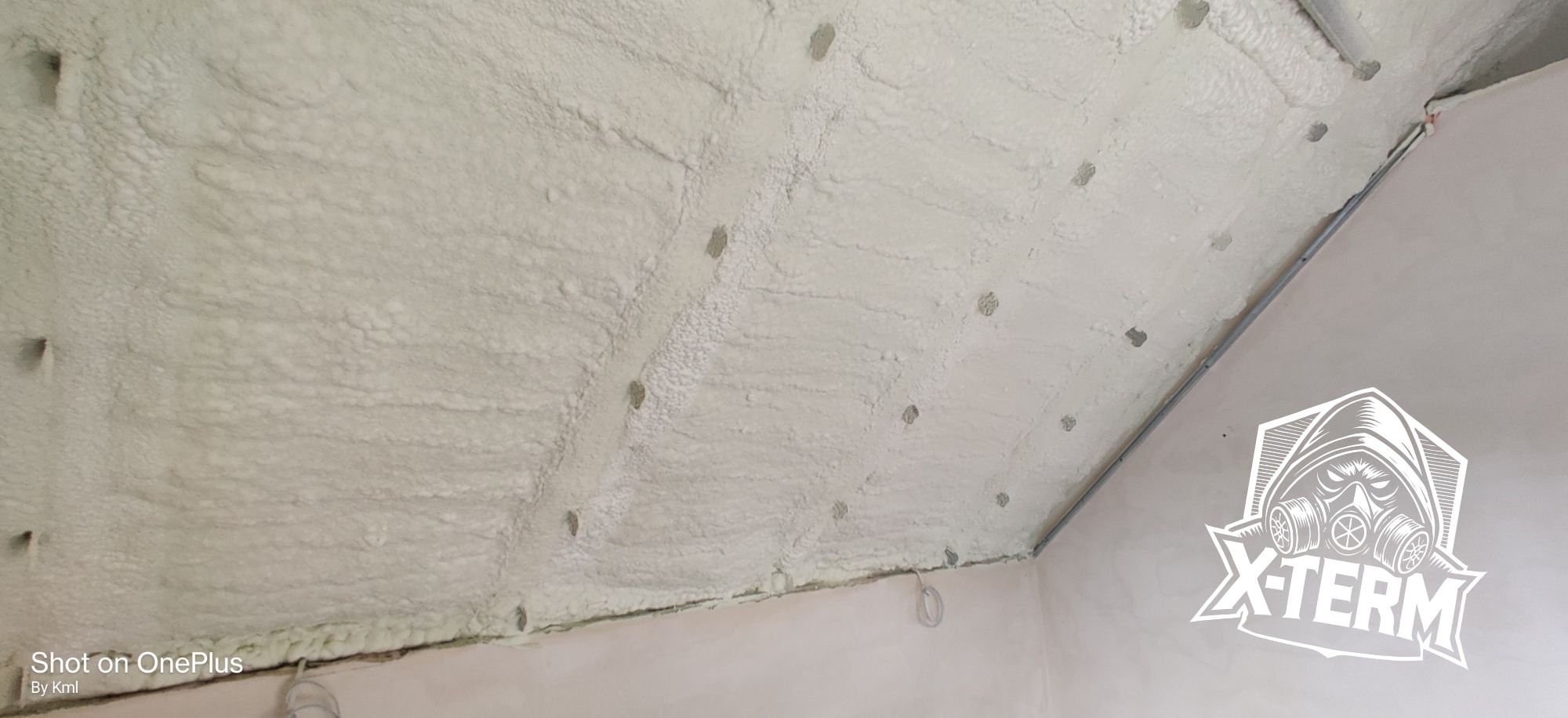 Poddasze po natrysku pianki izolacyjnej, widoczne otwory po kołkach montażowych, w rogu pomieszczenia logo firmy X-TERM.