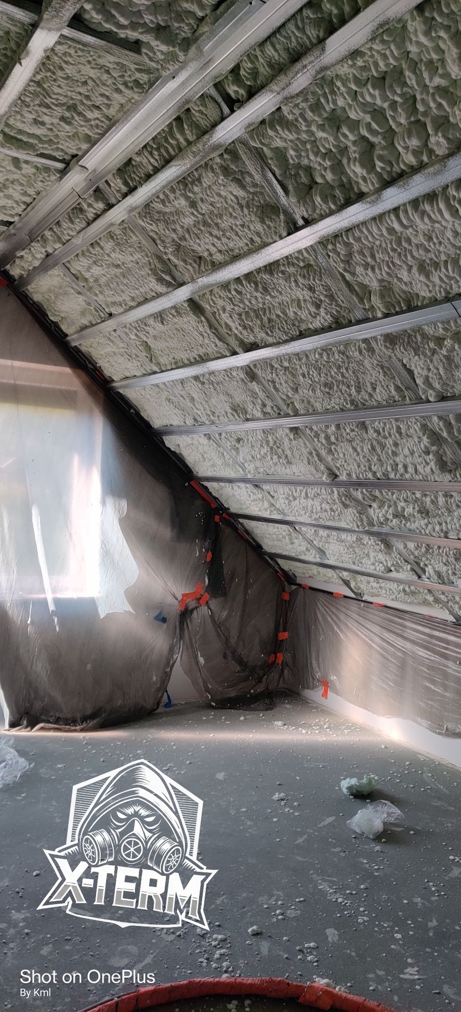 Poddasze z metalową konstrukcją i warstwą szarej pianki izolacyjnej, zabezpieczone folią ochronną przy ścianach.