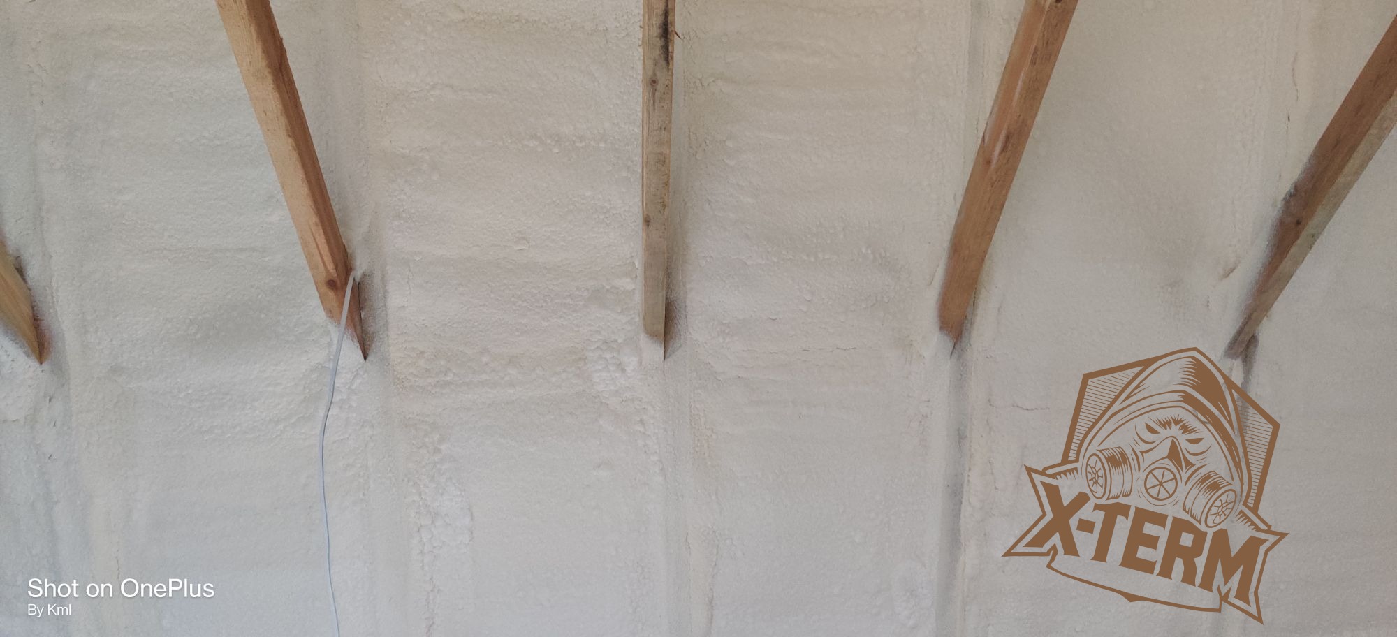 Poddasze z drewnianą konstrukcją pokryte białą pianką izolacyjną, widoczne logo X-TERM