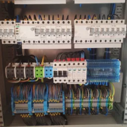 Rozdzielnica elektryczna z precyzyjnie ułożonymi kablami i zabezpieczeniami, widok z bliska na uporządkowane połączenia i komponenty.