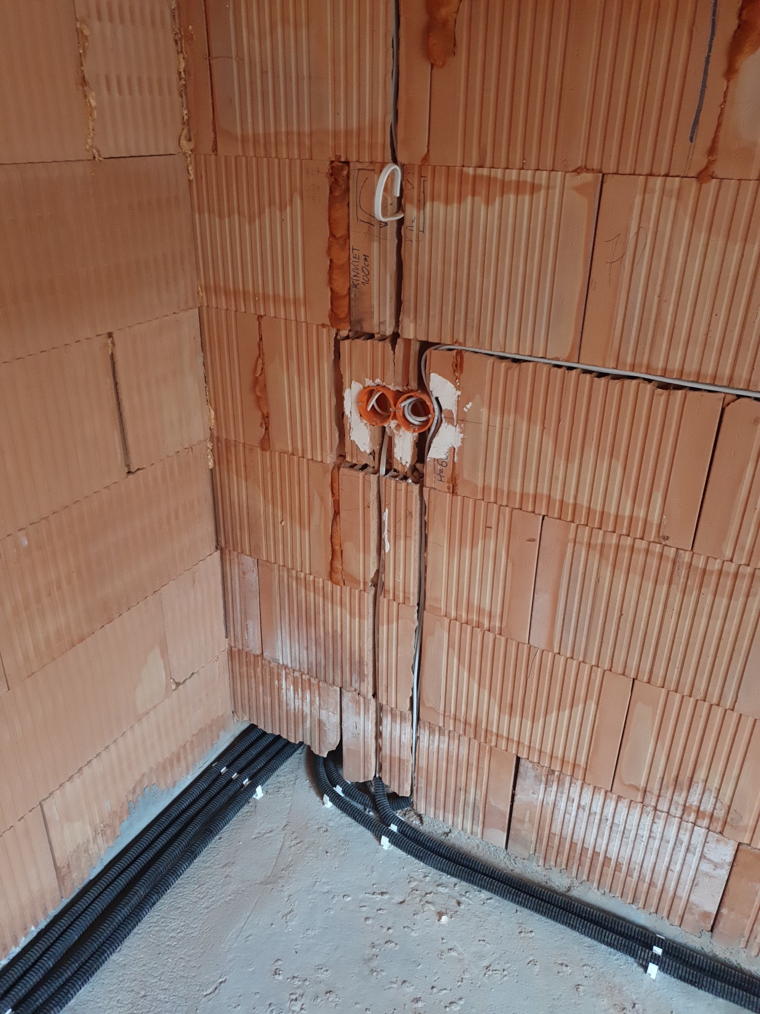 Wewnętrzna instalacja elektryczna w ścianie z pustaków ceramicznych, widoczne kable w peszlach oraz puszki instalacyjne.