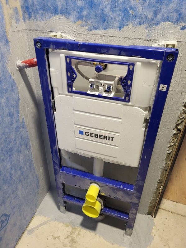 Stelaż podtynkowy Geberit zamontowany przy ścianie w łazience w trakcie remontu. Widoczne przyłącza i elementy instalacji. Ściany przygotowane pod glazurę.