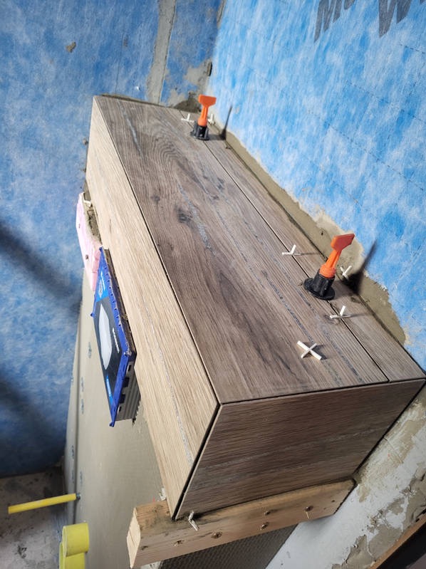 Półka obłożona płytkami imitującymi drewno, z użyciem systemu poziomowania płytek, na tle ściany z niebieską membraną hydroizolacyjną.