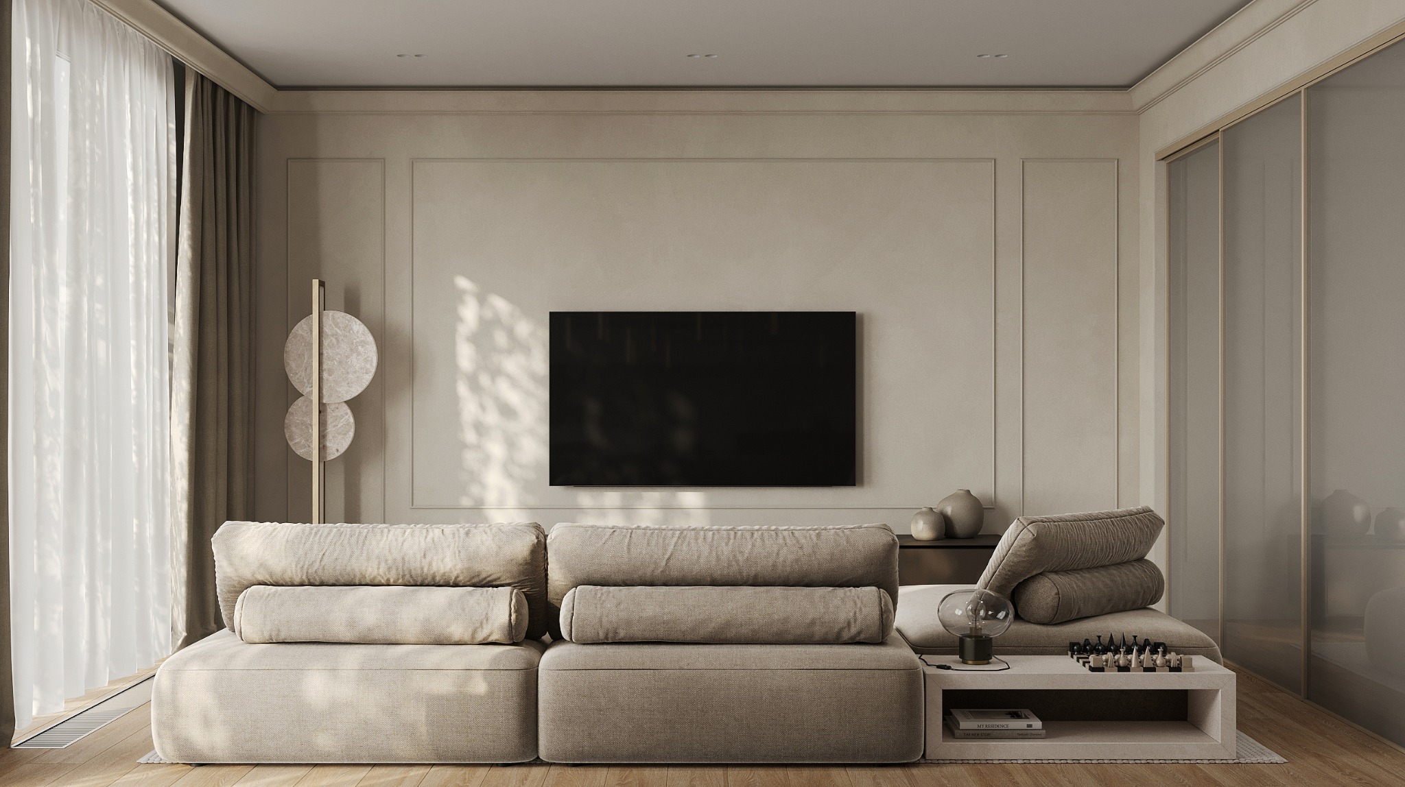 Beżowa sofa modułowa z podłużnymi poduszkami na tle ściany z telewizorem, obok stolik z lampą i szachami, oświetlona promieniami słońca wpadającymi przez okno z zasłonami.