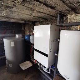 Tomasz Kowalik - Instalacja pompy ciepła Panasonic w piwnicy: zbiornik buforowy, zasobnik CWU Galmet, biała jednostka wewnętrzna. Widoczne rury i armatura. Surowy strop piwniczny.