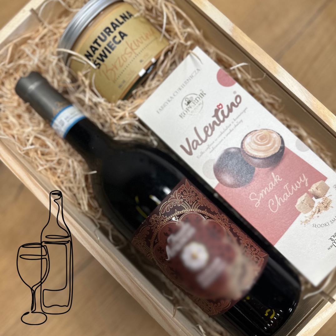 Drewniana skrzynka prezentowa wypełniona siankiem, zawierająca butelkę czerwonego wina z ozdobną etykietą, pudełko czekoladek 'Valentino' oraz świecę 'Naturalna Świeca Brzoskwinia'.