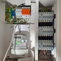 Robo Elektroinstalacje - Otwarta rozdzielnica elektryczna z licznikiem ISKRA, modułami Hager i ogranicznikiem przepięć Simtec, ukazująca precyzyjne okablowanie.