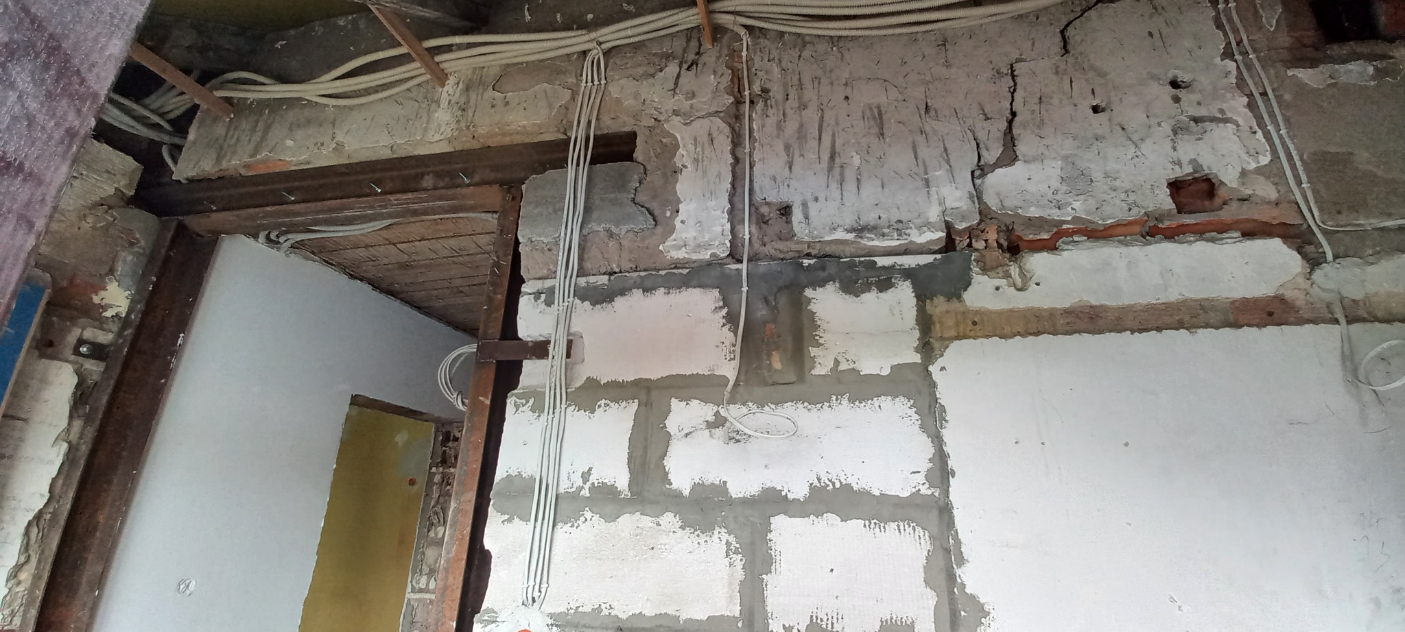 Przewody elektryczne prowadzone po ścianie z pustaków i pod sufitem w trakcie remontu, widoczne fragmenty starego tynku.