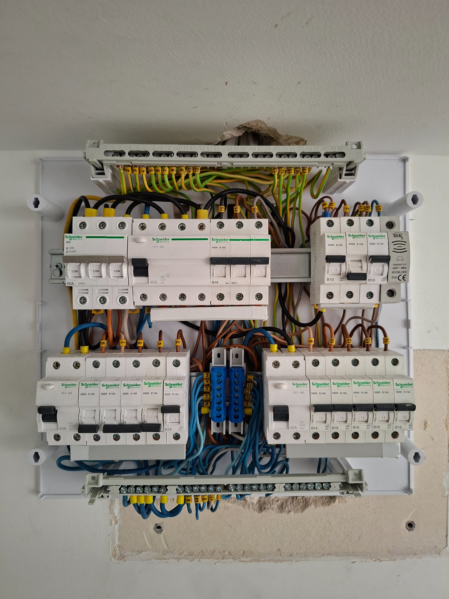 Starannie wykonana instalacja w otwartej rozdzielnicy elektrycznej Schneider Electric, z rzędami wyłączników i kolorowymi przewodami podłączonymi do listew.