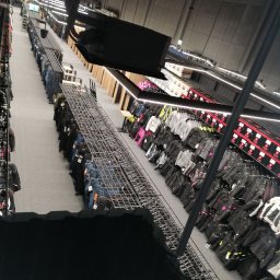 Sviatoslav Berezovskyi - Widok z góry na wnętrze sklepu z odzieżą i wyposażeniem, z rzędami wieszaków i półek wypełnionych produktami, oświetlonymi ledowymi lampami.