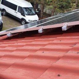 Sviatoslav Berezovskyi - Częściowo zamontowane panele fotowoltaiczne na czerwonym dachu z widocznym białym busem w tle, ujęcie z góry.