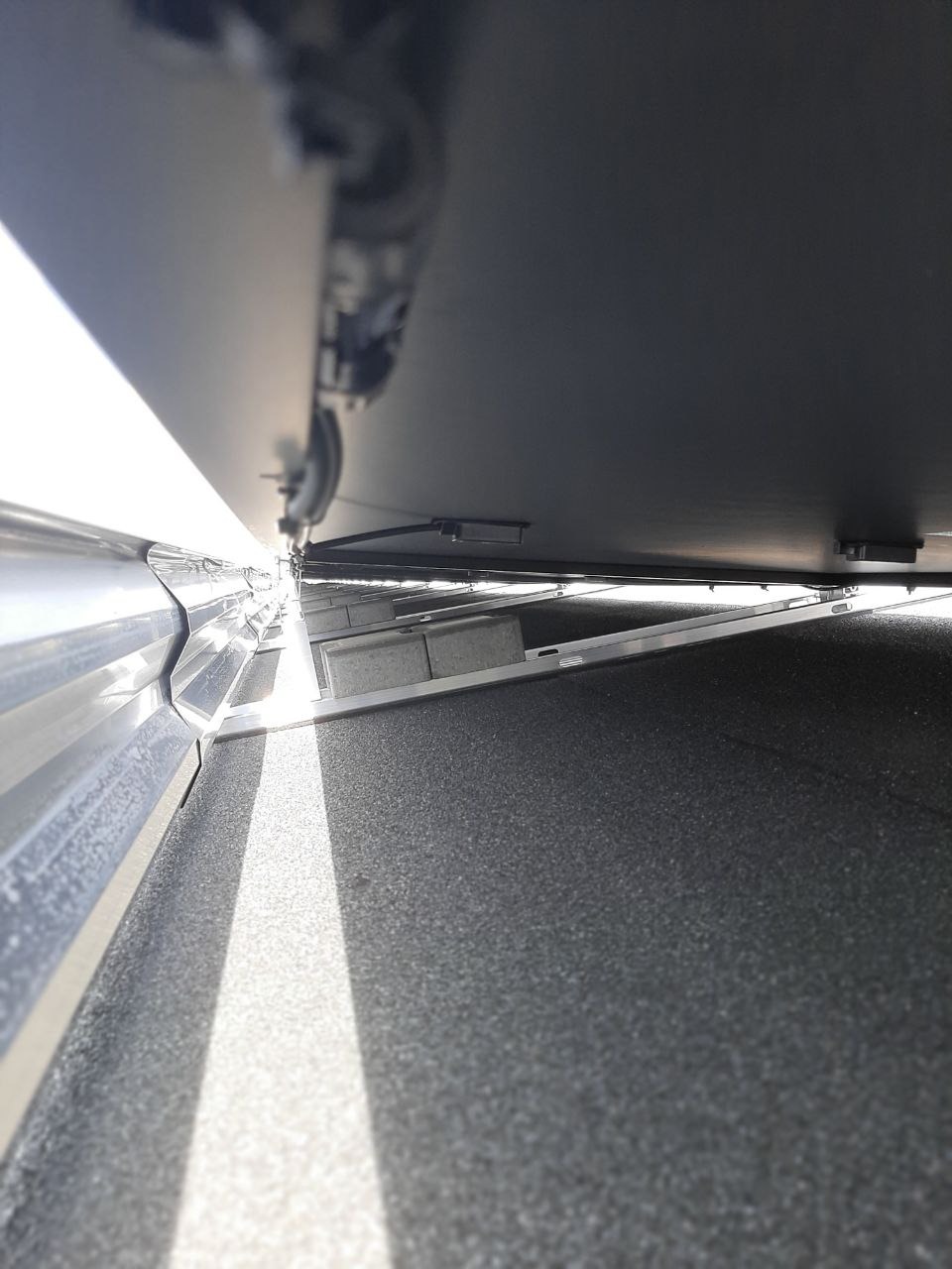 Widok z dołu na zamontowaną bramę garażową z widocznym mechanizmem otwierania i fragmentem posadzki w garażu, oświetlonym przez szczelinę w bramie.