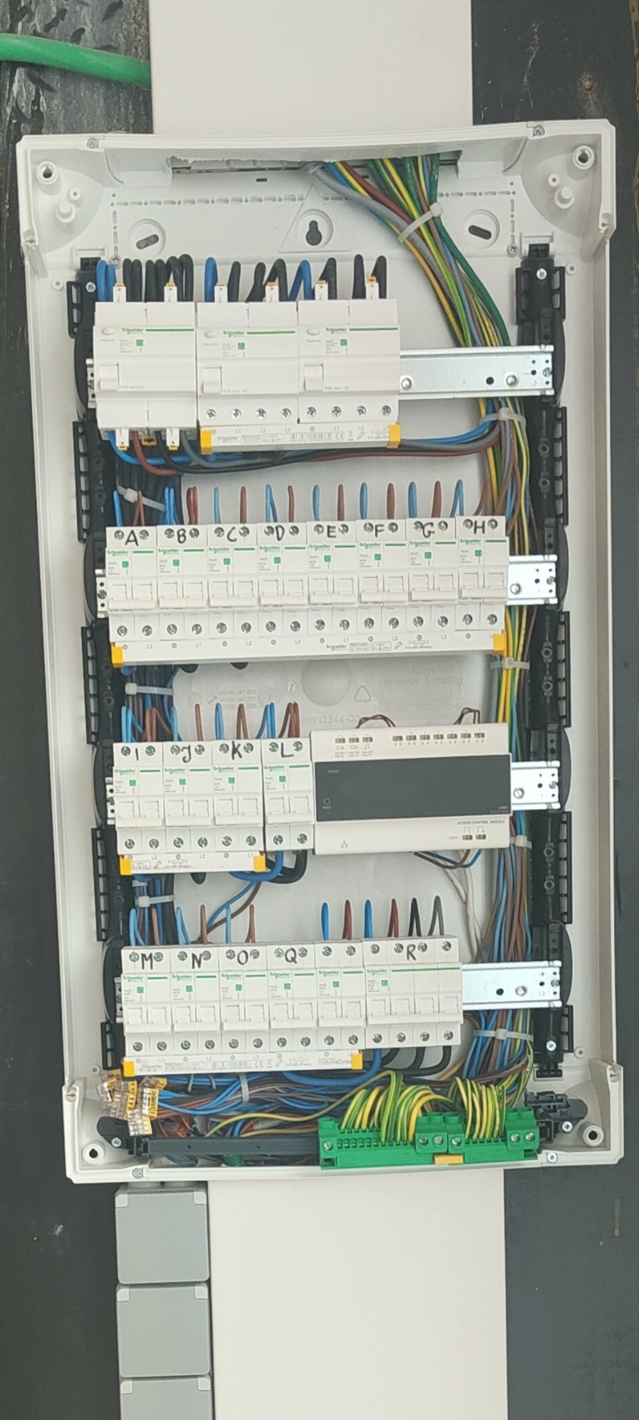 Otwarta skrzynka rozdzielcza z zainstalowanymi bezpiecznikami i przewodami oznaczonymi literami A-R, widoczne złącza WAGO i moduł sterujący.