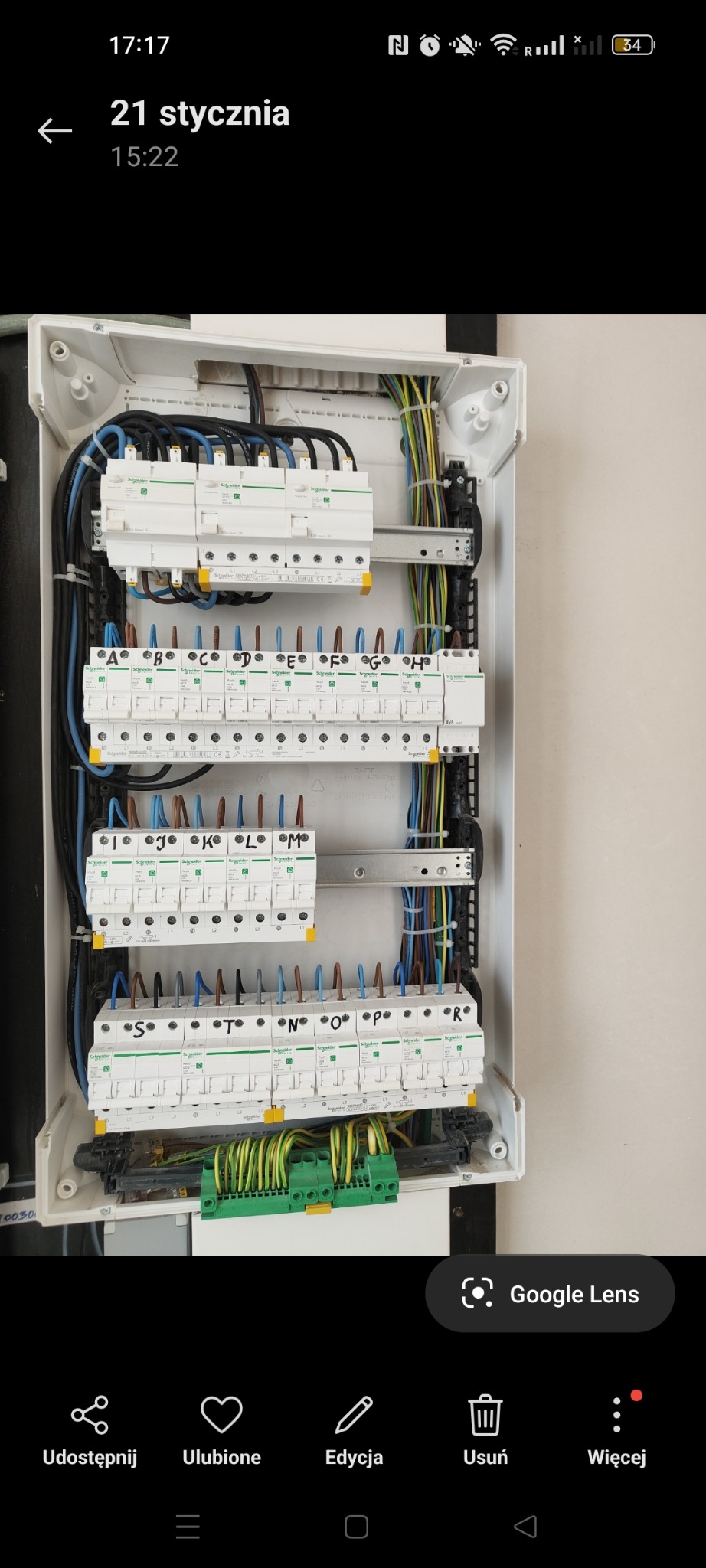 Rozdzielnica elektryczna z zainstalowanymi bezpiecznikami i przewodami oznaczonymi literami od A do R, widoczne złącza szynowe i przewody ochronne w kolorze zielono-żółtym, montaż w białej obudowie.