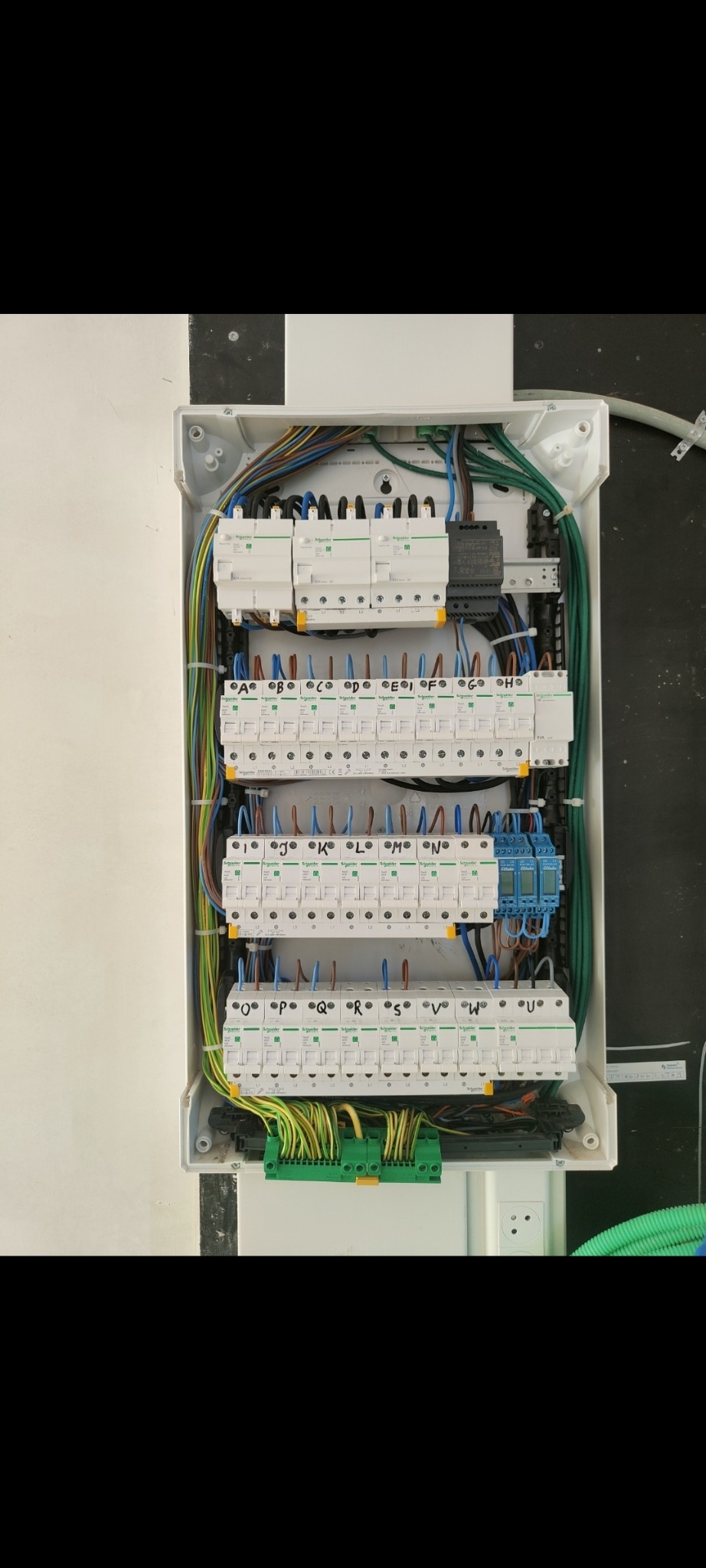 Otwarta skrzynka rozdzielcza z bezpiecznikami i okablowaniem, widoczne oznaczenia literowe na bezpiecznikach.