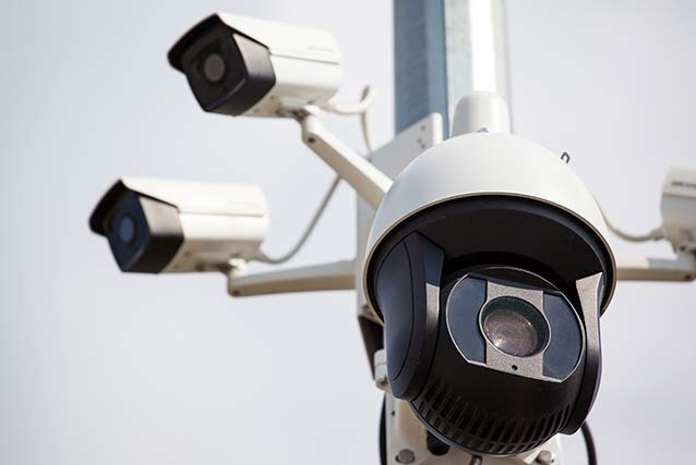 Zestaw kamer monitoringu na słupie, różne typy, w tym obrotowa, skierowane w różne strony, na tle jasnego nieba.