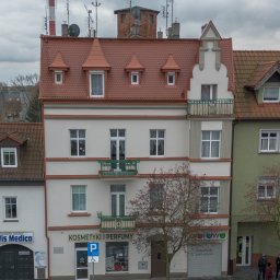 DomVisio - Trzypiętrowy budynek z balkonami i sklepem 'Kosmetyki i Perfumy' na parterze, widok z góry na parking dla niepełnosprawnych i zaparkowany czarny samochód.