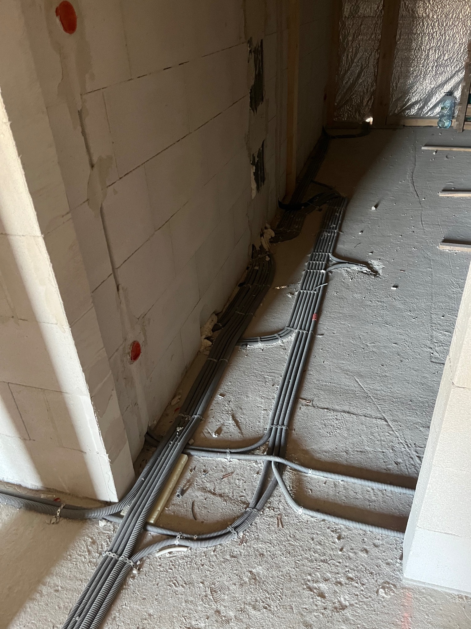Szare rury instalacji elektrycznej ułożone wzdłuż ściany z pustaków w surowym wnętrzu budynku w Tokarni, widoczne puszki instalacyjne.