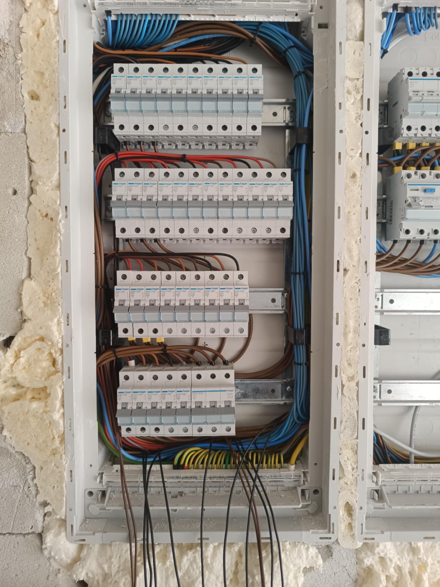Rozdzielnica elektryczna z zabezpieczeniami i okablowaniem, zamontowana w ścianie z widoczną pianką montażową.