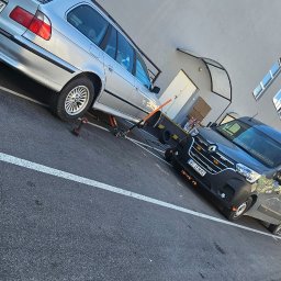 Mobilna wulkanizacja płock 24h7 Paradowski Marcin - Srebrne kombi BMW na podnośniku hydraulicznym, bez koła, obok czarna laweta Renault z włączonymi pomarańczowymi światłami ostrzegawczymi, na parkingu z widocznymi śladami opon.