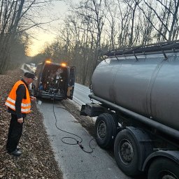 Mobilna wulkanizacja płock 24h7 Paradowski Marcin - Serwis mobilny przy cysternie: mężczyzna w kamizelce odblaskowej podłącza przewód z agregatu prądotwórczego w busie do instalacji cysterny na poboczu drogi w lesie.