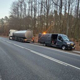 Mobilna wulkanizacja płock 24h7 Paradowski Marcin - Awaryjne holowanie cysterny na poboczu drogi, z otwartymi drzwiami busa serwisowego i włączonymi światłami ostrzegawczymi, w tle las bez liści.