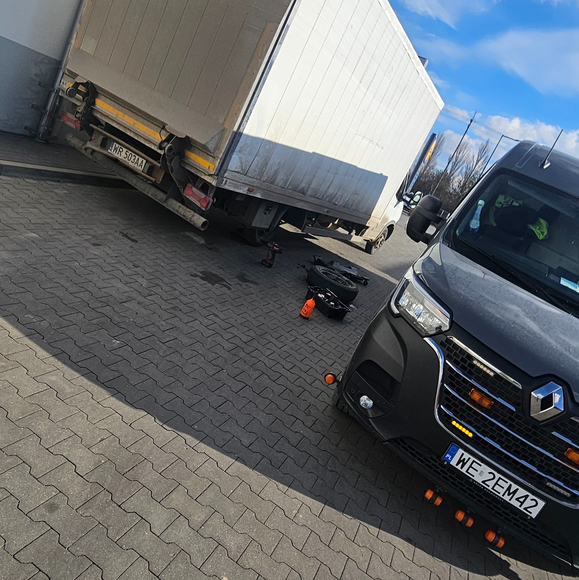 Tir na parkingu z odkręconym kołem, obok leżą narzędzia i czarne auto dostawcze marki Renault z polską rejestracją WE 2EM42.