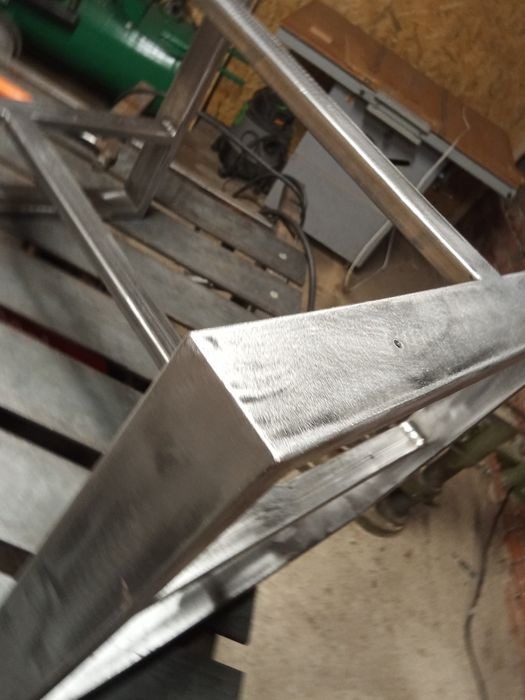 Metalowa konstrukcja ramy, prawdopodobnie elementu mebla, spawana i częściowo obrobiona, widoczna w warsztacie.