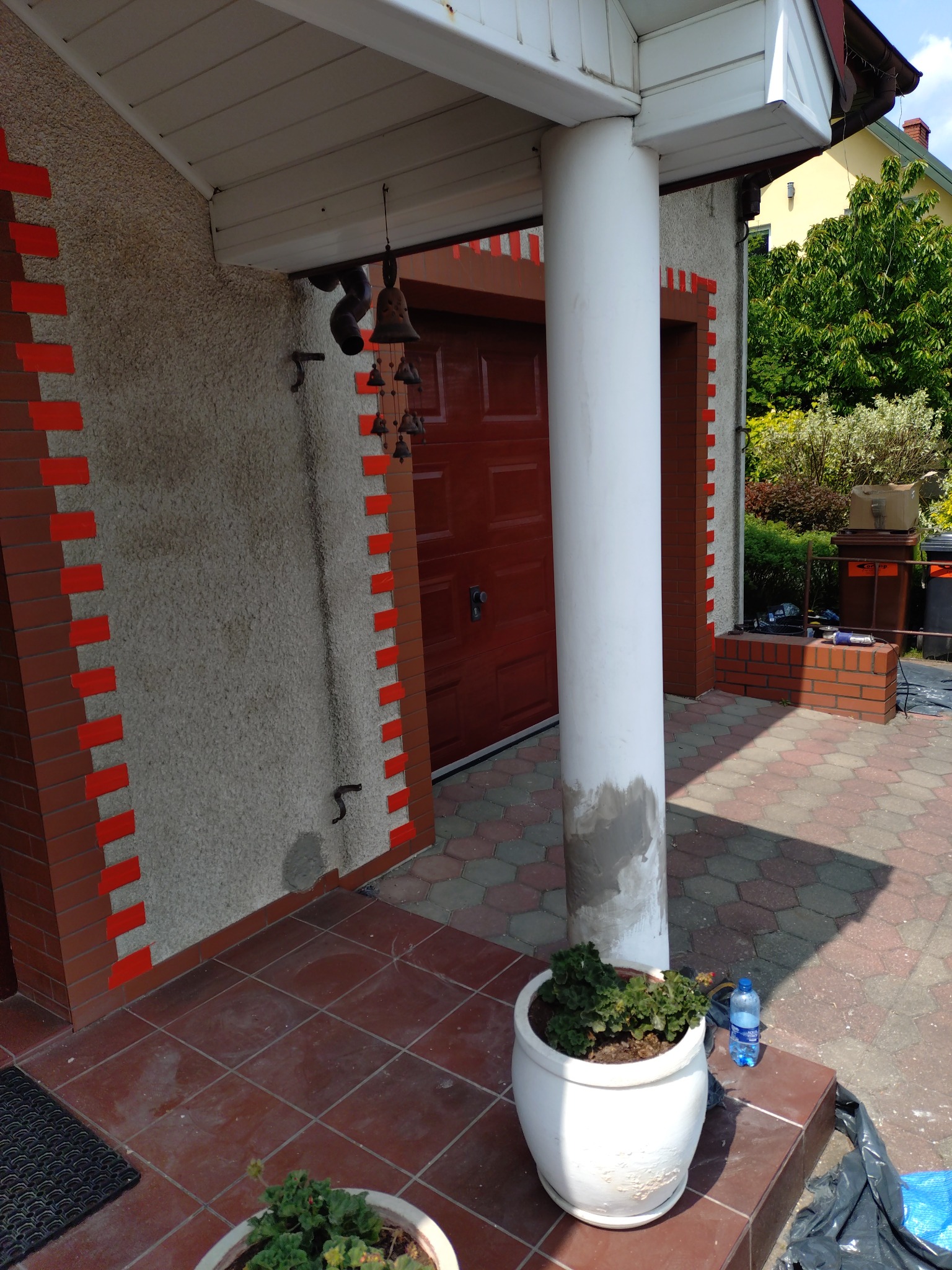 Wejście do budynku przed remontem: ściana z fakturą i dekoracyjnym obramowaniem imitującym cegłę. Widoczny fragment kolumny i drzwi wejściowe.