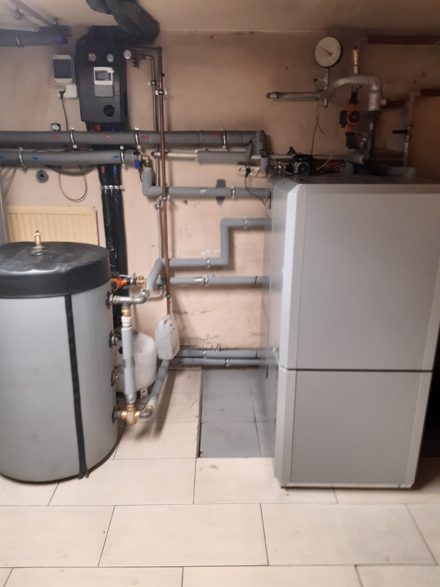 Nowoczesny piec grzewczy z zasobnikiem w kotłowni w Lublinie, widoczne rury instalacji grzewczej i wodnej.