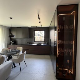 Dmytro Tytorenko - Nowoczesna kuchnia z ciemnymi frontami i podświetlaną szafką na wino. Okrągły stół z krzesłami w jasnej tonacji. Minimalistyczny design, eleganckie wykończenie.