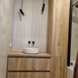 Ma&Ja Meble - Nowoczesna łazienka z szafką pod umywalką w odcieniach drewna, okrągłą białą umywalką nablatową i dwoma czarnymi lampami sufitowymi.