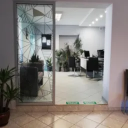 Wnętrze biura w Nowej Rudzie z recepcją i stanowiskami pracy, widoczne przez przeszklone drzwi z geometrycznym wzorem. Rośliny doniczkowe dodają naturalnego akcentu.