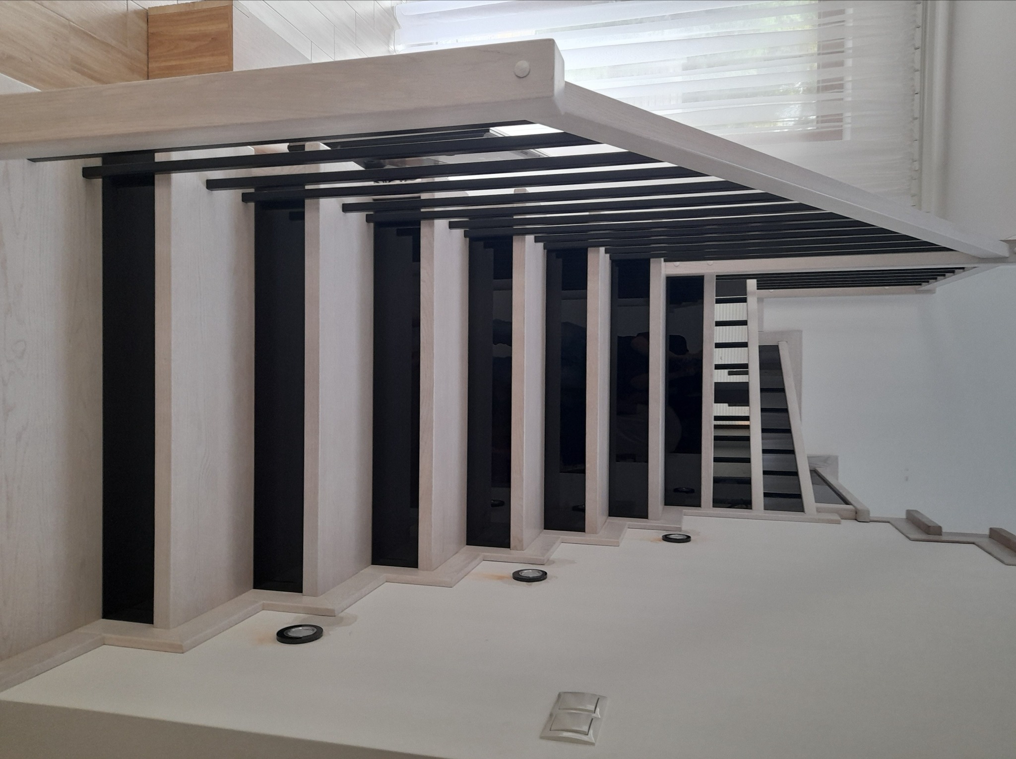 Nowoczesne schody z jasnego drewna i czarnymi elementami, zintegrowane oświetlenie punktowe w podstopnicach, widok z góry.