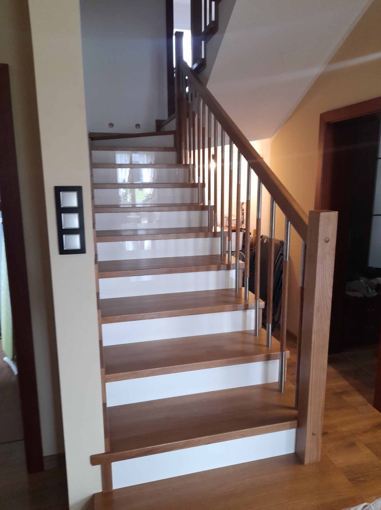 Nowoczesne schody z drewnianymi stopniami i białymi podstopnicami, balustrada ze stali nierdzewnej i drewnianymi słupkami, widok z dołu.