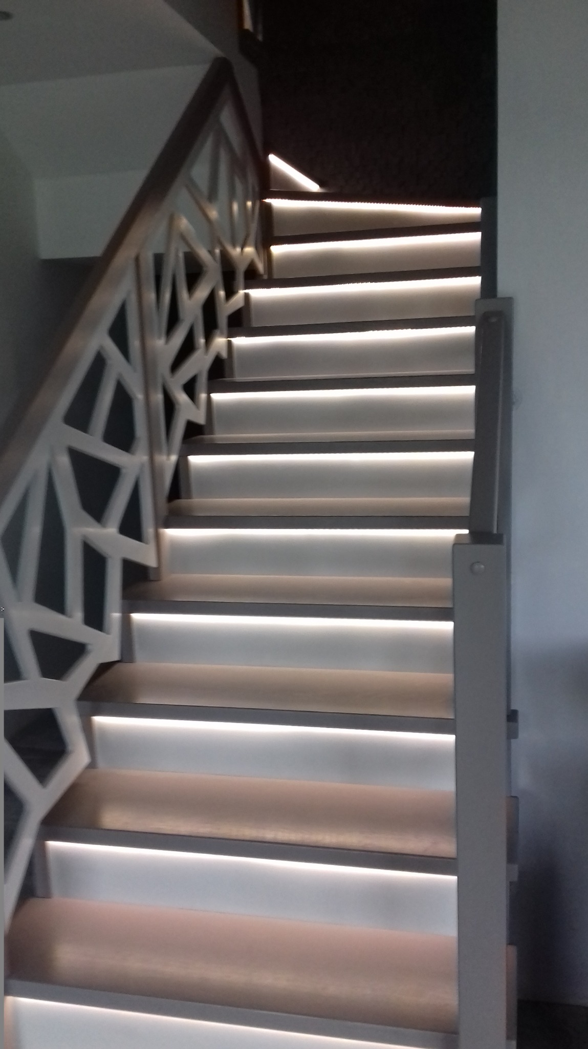 Nowoczesne schody z podświetleniem LED pod każdym stopniem, z ażurową balustradą w geometryczne wzory.