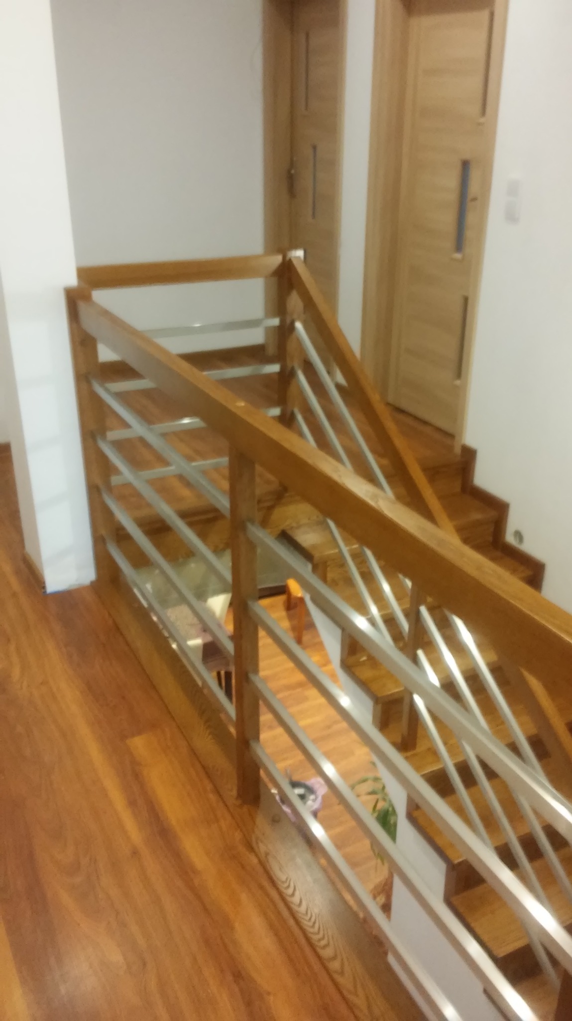 Drewniane schody z metalowymi balustradami, widok z góry na dół, z dwiema parami drzwi w tle.