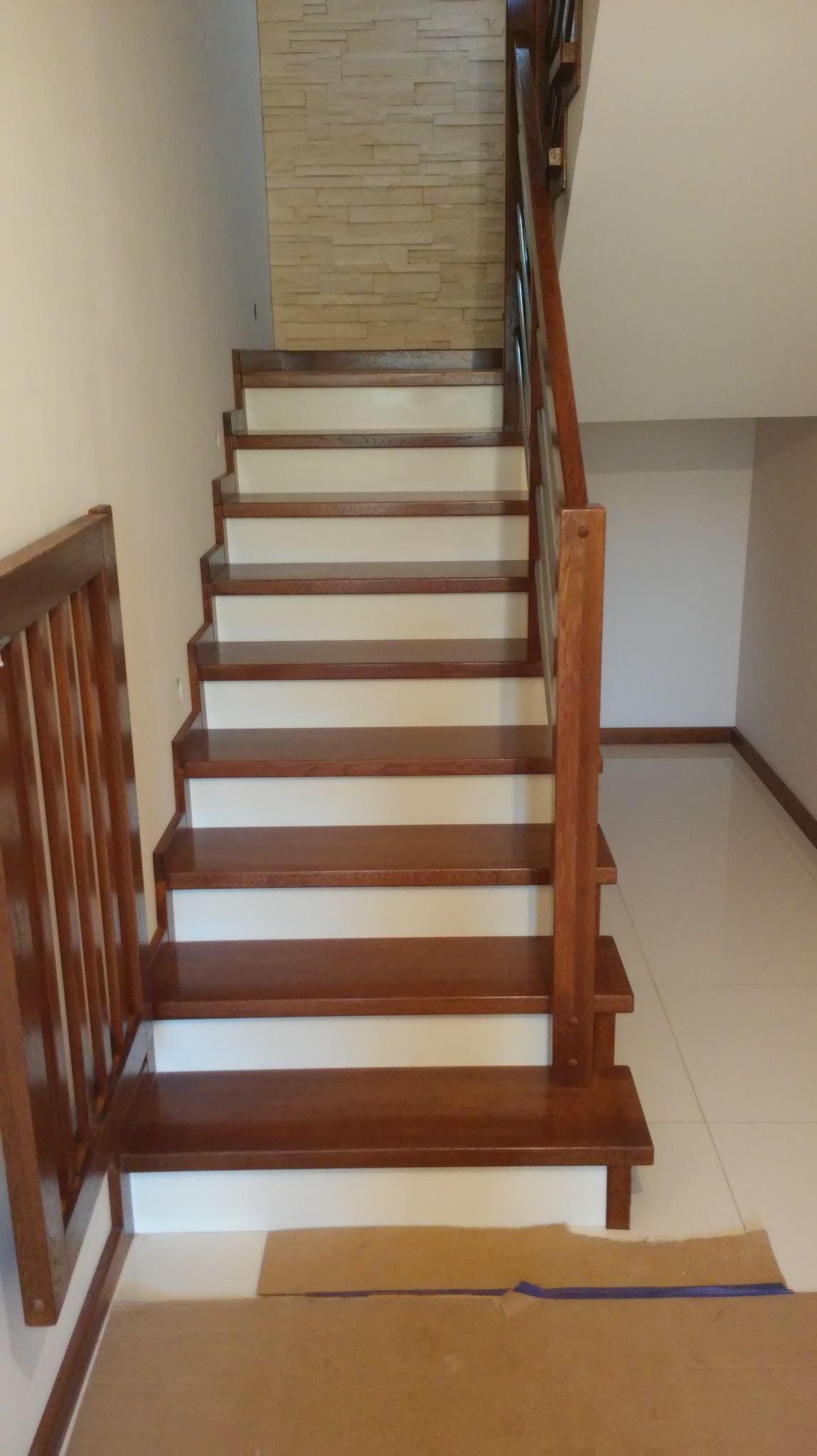 Klasyczne schody z drewnianymi stopniami i białą podstopnicą, zabezpieczone kartonem na podłodze podczas prac wykończeniowych.