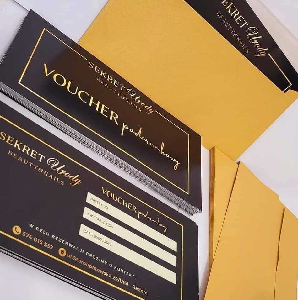 Stos czarno-złotych voucherów podarunkowych z danymi do wypełnienia, obok koperty w kolorze złota, z logo 'Sekret Urody Beauty&Nails'.