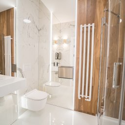 ROBERT JANCZURA PERFECTLIFT - Nowoczesna łazienka z marmurowymi i drewnianymi płytkami, białą umywalką nablatową, grzejnikiem drabinkowym i kabiną prysznicową ze szklanymi drzwiami.