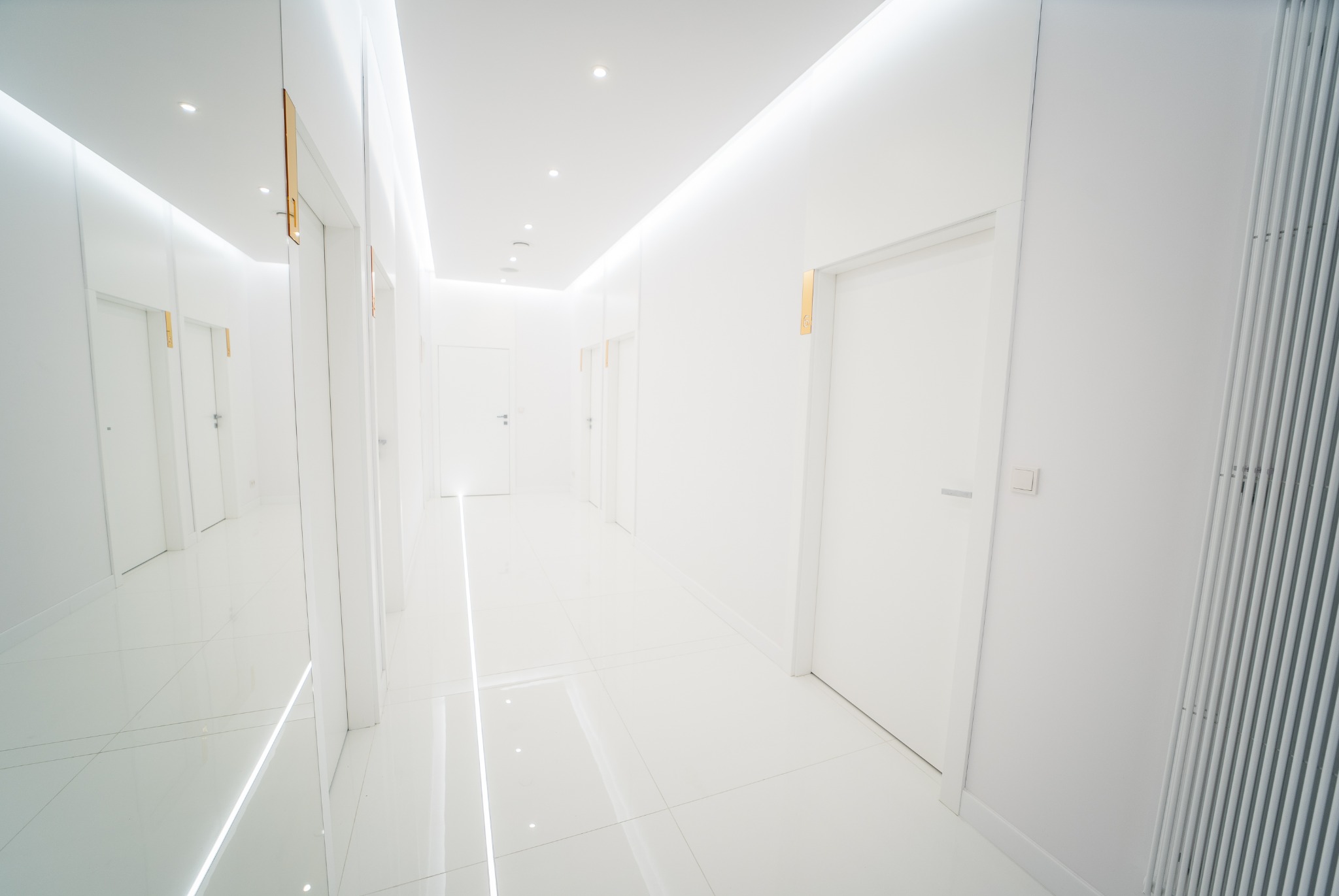 Jasny, minimalistyczny korytarz w klinice z białymi ścianami, drzwiami z numerami i błyszczącą podłogą.