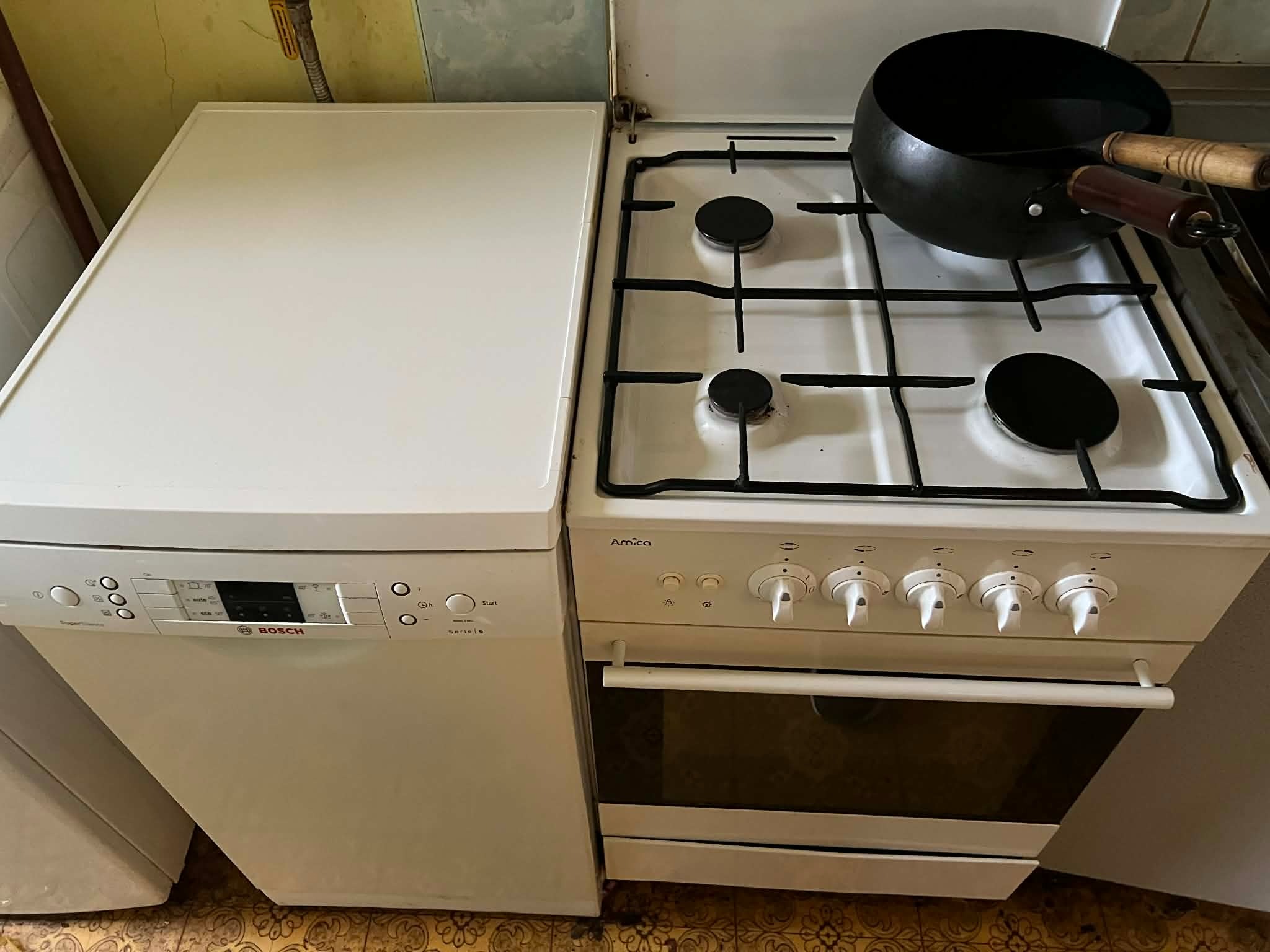 Biała kuchnia Amica z garnkiem i zmywarka Bosch Serie 6. Widok z góry na sprzęty AGD w kuchni. Na podłodze wzorzyste linoleum.