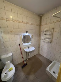 Umywalka, toaleta i wanna w wykafelkowanej łazience po sprzątaniu. Widoczne rury i grzejnik drabinkowy. Na toalecie leżą rolki papieru i gąbka.