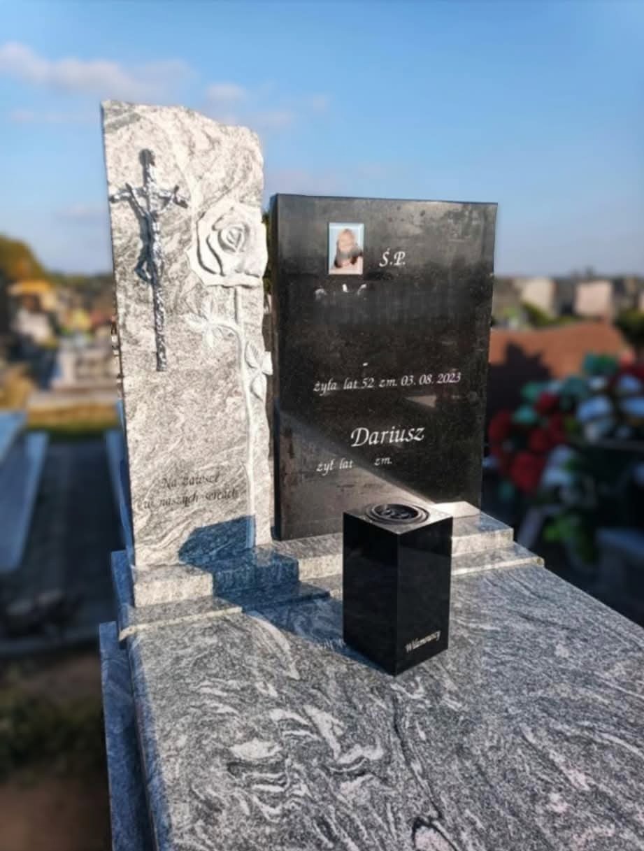 Granitowy nagrobek z rzeźbionym krzyżem i różą, czarna tablica z portretem i datami, oraz czarny znicz; widok na cmentarz w tle.
